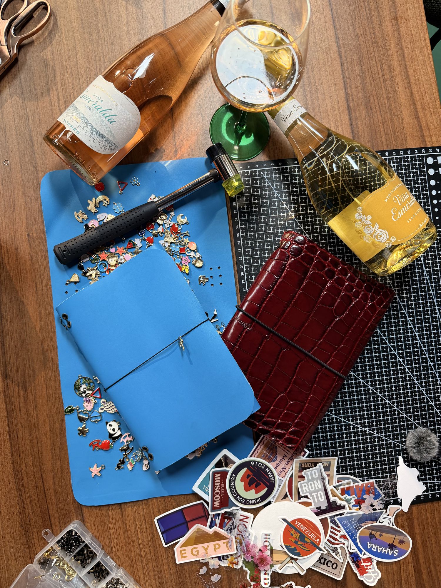 Cuadernos de piel, charms, pegatinas y vino sobre la mesa del taller